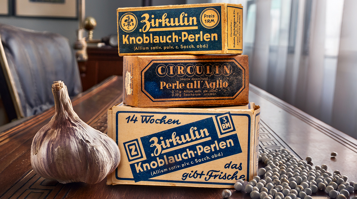 Drei Vintage-Schachteln mit Knoblauchperlen auf einem Tisch, gestapelt neben einer Knoblauchknolle und verstreuten Perlen. Die Schachteln sind mit deutschen und italienischen Texten sowie Motiven im Retro-Stil versehen.